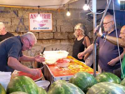 Quando arriviamo troviamo l�uomo intento a tagliare fette di melone rosso per i numerosi clienti in fila, proprio accanto all�insegna che recita: �Angurie fresche da Donato�